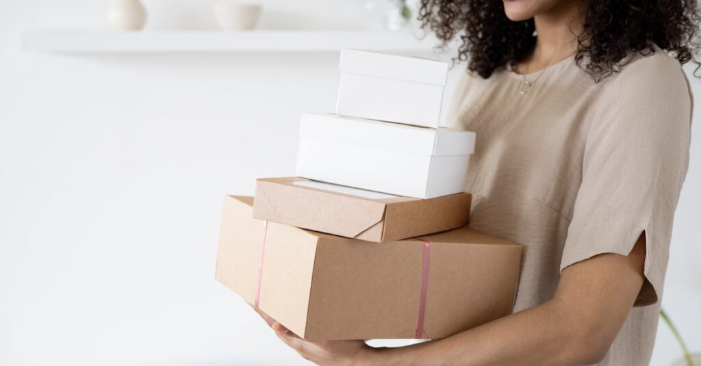 Woman with curly hair carrying stack of packaging boxes in a bright room.