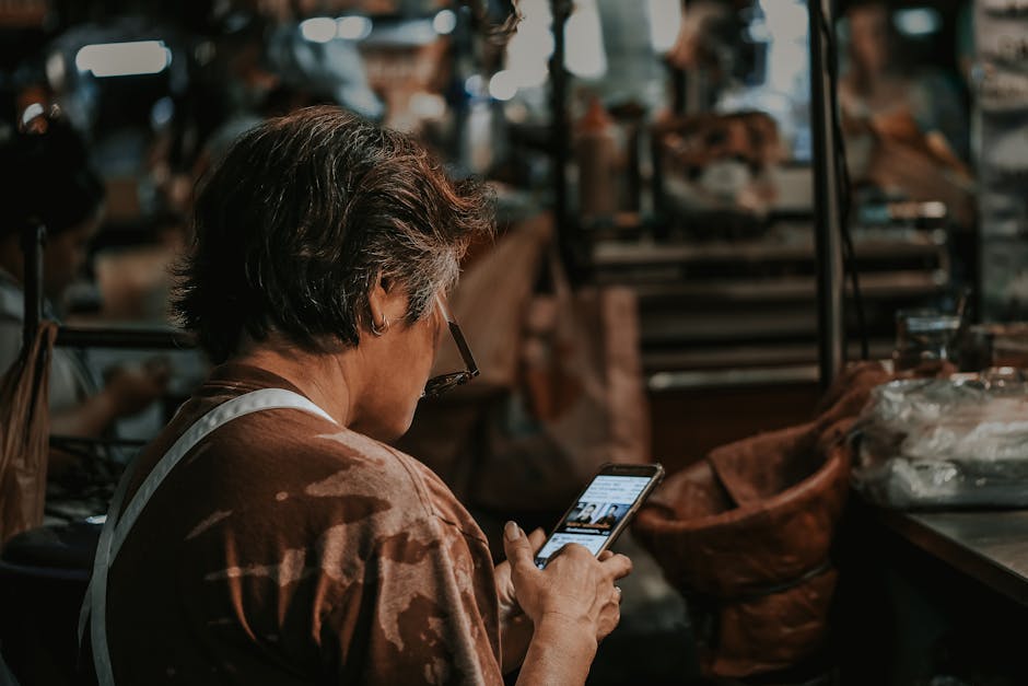 A woman with short hair looking down at a smartphone in a busy market environment.